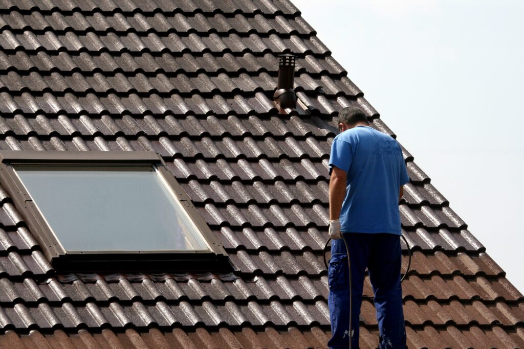 Ein Handwerker in blauer Arbeitskleidung arbeitet auf einem Dach mit Ziegeln und Dachfenster.